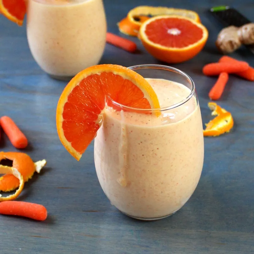 Orange and Carrot Smoothie with Ginger and Turmeric with ingredients on blue background