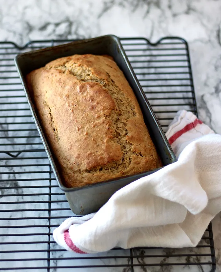Banana bread in the pan on a cooling rack with a towel