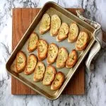 Toasted crostini on pan sitting on cutting board