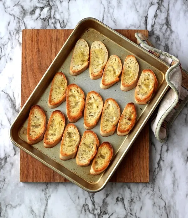 Toasted crostini on pan sitting on cutting board
