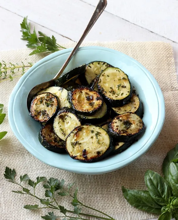 grilled zucchini slices in a teal bowl on a white background