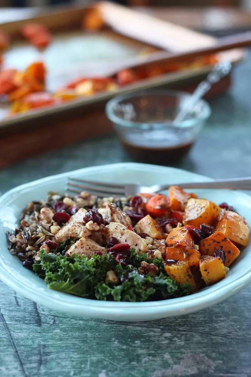 kale, wild rice, chicken, and winter veggies in teal bowl with pan of veggies in background