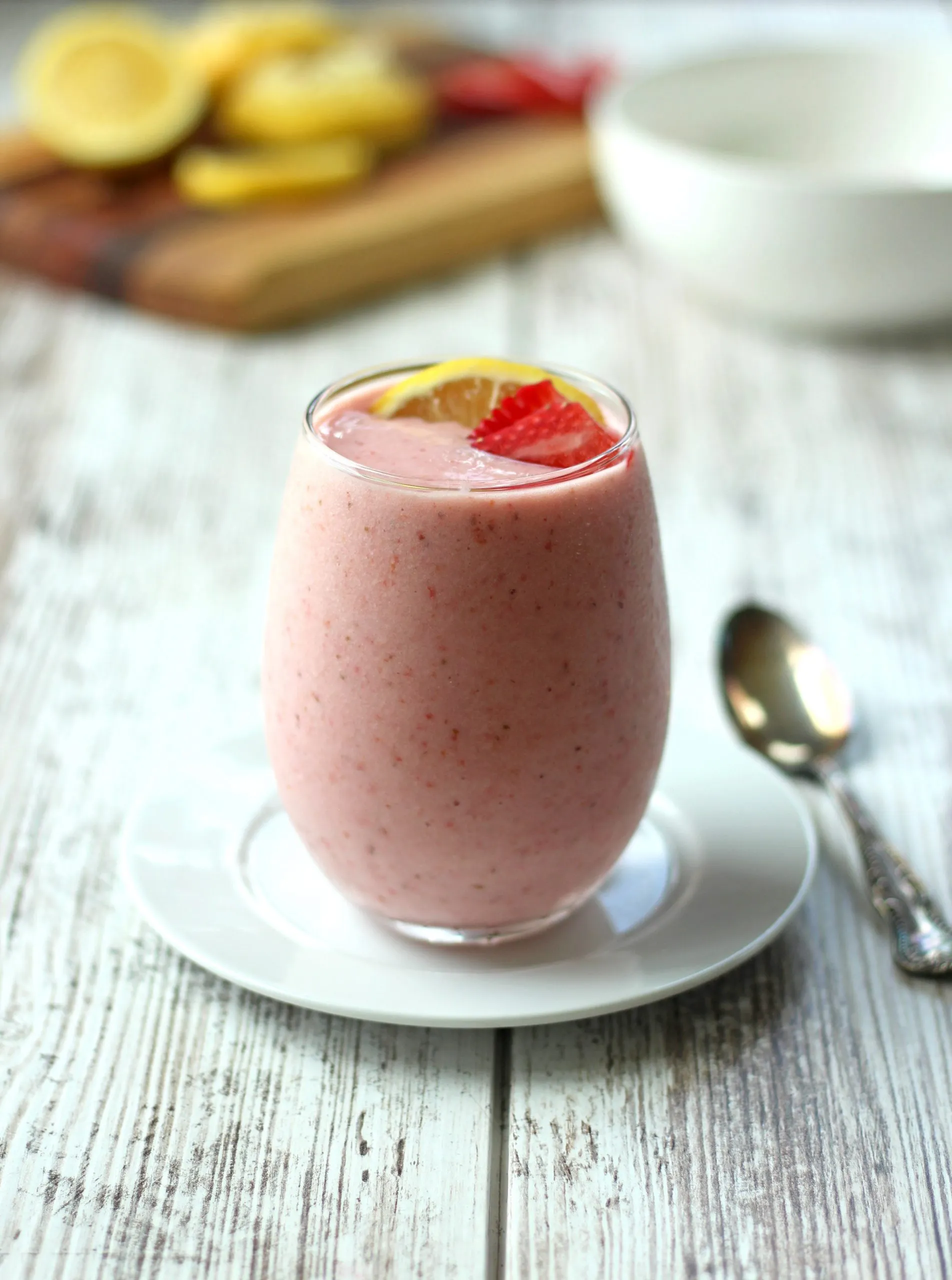 pink smoothie with strawberries and lemon slices on cutting board in background
