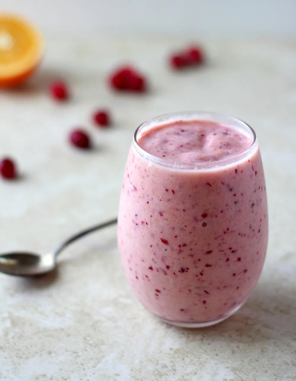 Cranberry and orange smoothie in a clear glass against a white background