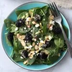 Blackberry spinach salad with feta cheese and sliced almonds on teal plate looking from above.