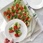 cucumber and hummus appetizer on white plate held above a tray of them