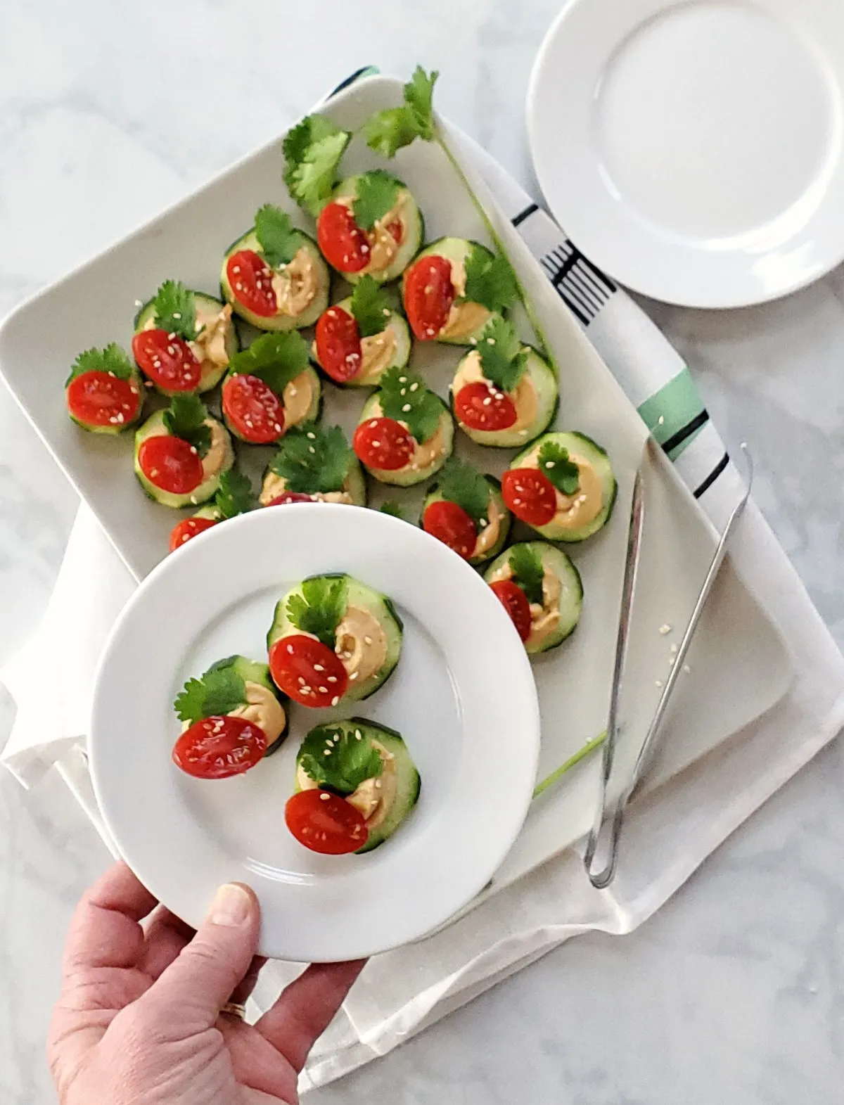 cucumber and hummus appetizer on white plate held above a tray of them
