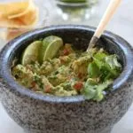 Guacamole in stone bowl with chips and cucumber in background