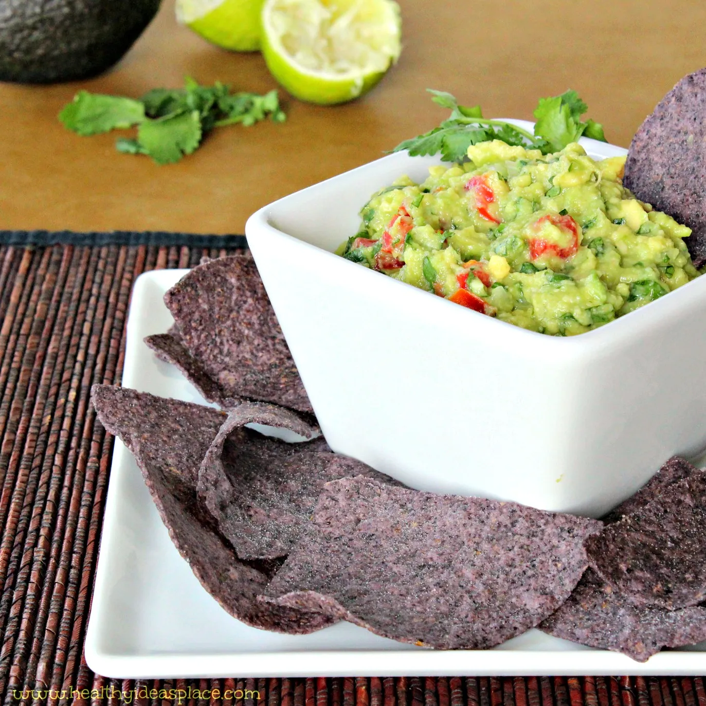 Guacamole and blue corn chips with a juiced lime in the background