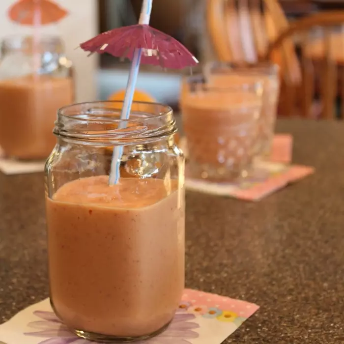 A Strawberry - Mango smoothie in a clear glass with an umbrella straw