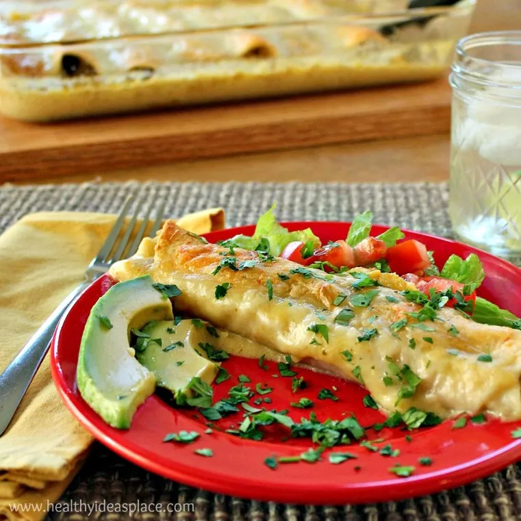 Chicken and Spinach Enchiladas on a red plate in the foreground with the baking dish behind