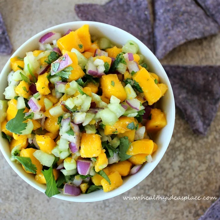 a bowl of Cucumber Mango Salsa with blue chips in the background