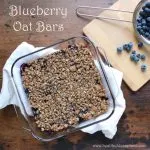 Blueberry Oat Bars in a clear baking dish next to a colander containing blueberries