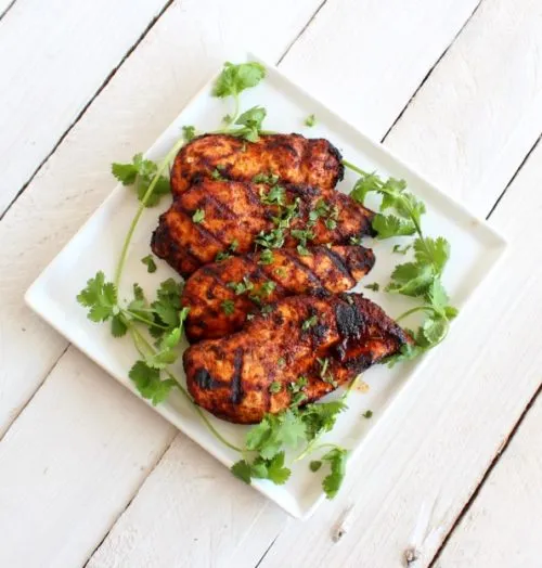 Cooked chicken breasts with fresh cilantro on white plate