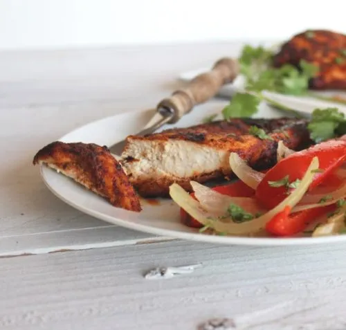 grilled chicken breast with onions and peppers on white plate