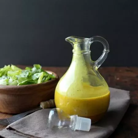 Apple Cider Turmeric Vinaigrette in a cruet next to a wooden bowl containing salad