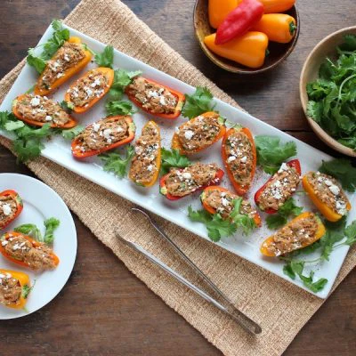 Southwest Tuna Stuffed Mini Peppers on a serving tray with a bowl of mini peppers and a bowl of greens