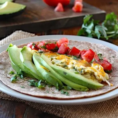 Breakfast Burrito with Eggs, Tomato, and Avocado on a white plate ready to be rolled up