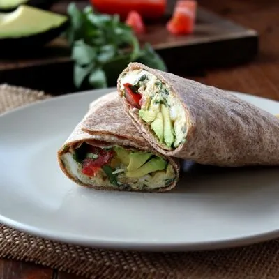 Closeup of a Breakfast Burrito with Eggs, Tomato, and Avocado on a white plate
