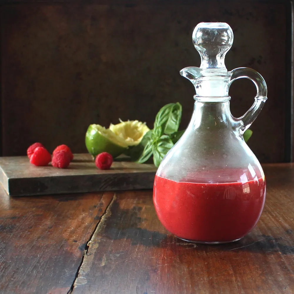 Raspberry Basil Vinaigrette in a cruet in front of cutting board containing the recipe ingredients