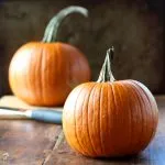 Two small pumpkins sitting on a wooden table with a knife