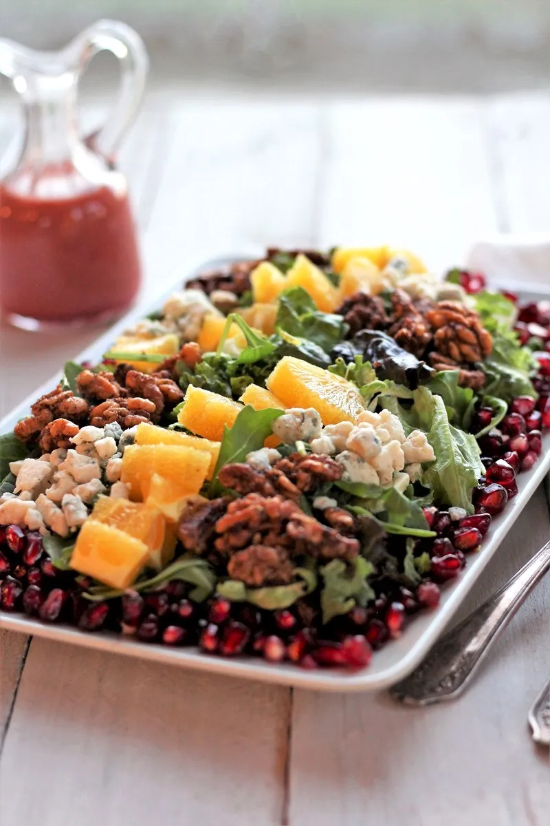 Spinach, Arugula and Pomegranate Salad in the foreground with Cranberry Citrus Vinaigrette in a bottle behind