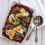 Spinach, Arugula & Pomegranate Salad on a table with napkin and utensils