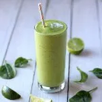 Green Smoothie with Pineapple and Mango with a straw and some limes scattered around