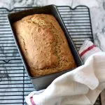 Banana bread in the pan on a cooling rack with a towel