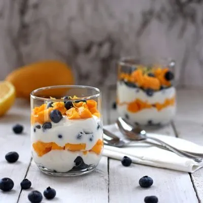 Diced mango and fresh blueberries layered with plain Greek yogurt in a clear glass