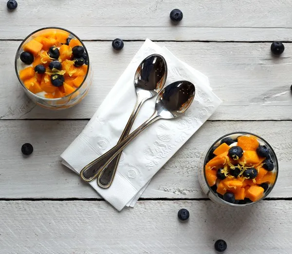 Top view of diced mango and fresh blueberries on top of Greek yogurt in a clear glass