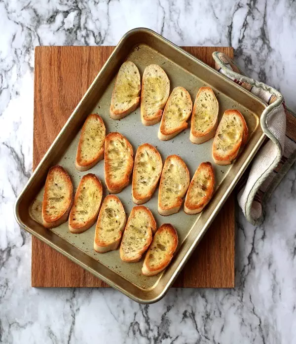 Toasted crostini on pan sitting on cutting board