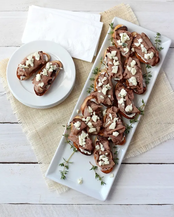 Overhead photo of roast beef, fig, and blue cheese crostini on white platter