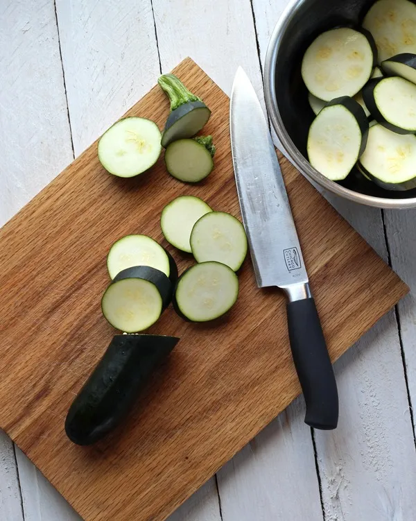 zucchini being sliced on wooden cutting board