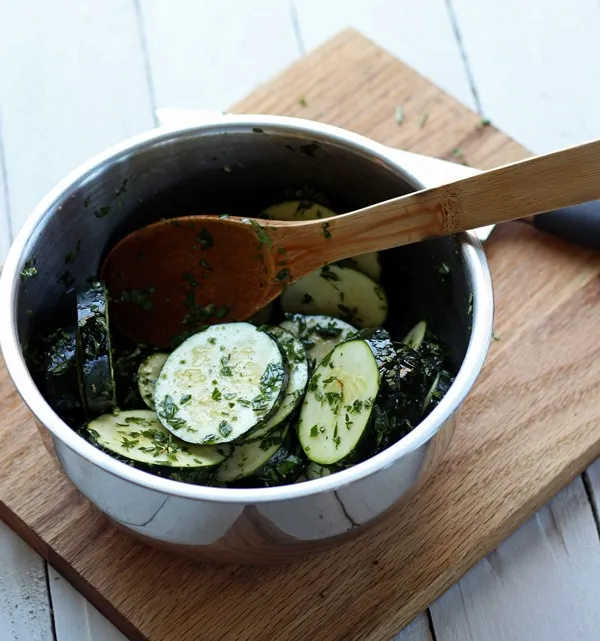 sliced zucchini and chopped fresh herbs in a metal bowl on a wood cutting board