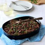 Quinoa stuffing in black dish on blue cloth with glasses on wine in background