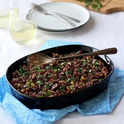 Quinoa stuffing in black dish on blue cloth with glasses on wine in background