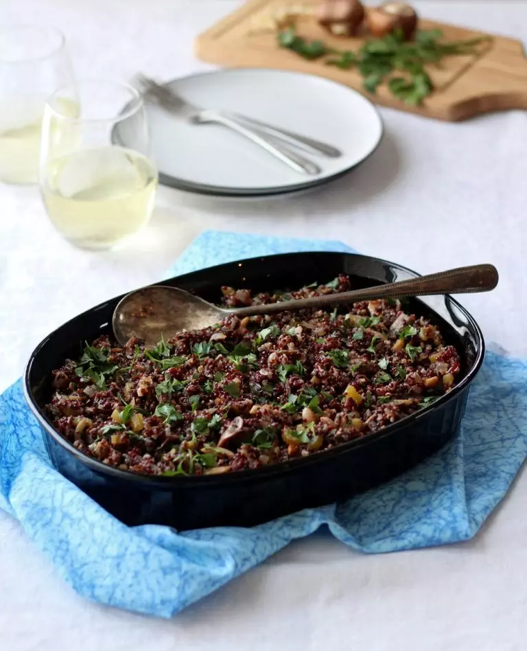 Quinoa stuffing in black dish on blue cloth with glasses on wine in background