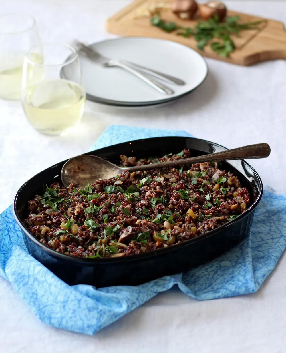 Quinoa stuffing in black dish on blue cloth with glasses on wine in background