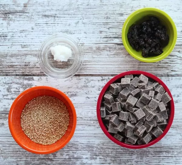 Coconut oil, dried cherries, dry quinoa, and dark chocolate chips in bowls on white wood background