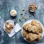 Baked scones on a white plate with a small bowl of walnuts nearby