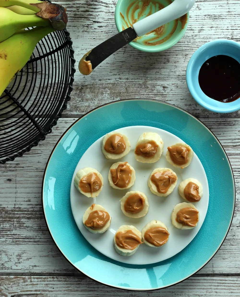 Slices on banana topped with peanut butter on white plate