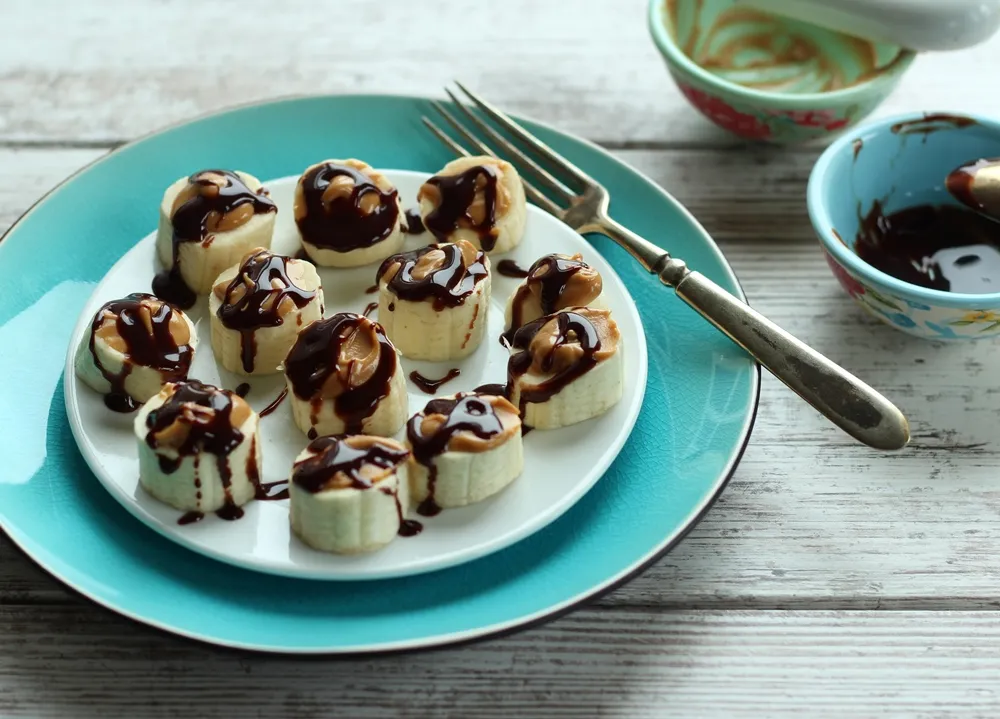 Banana slices topped with peanut butter and chocolate on white plate