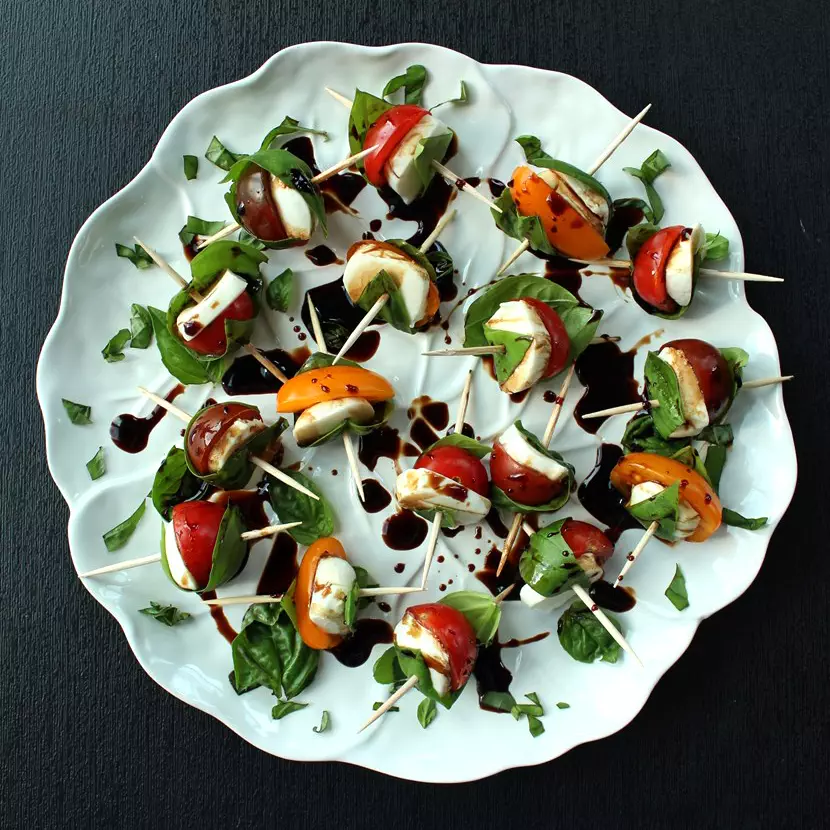 looking down on white plate with skewers of cherry tomatoes and fresh mozzarella wrapped with fresh basil leaves