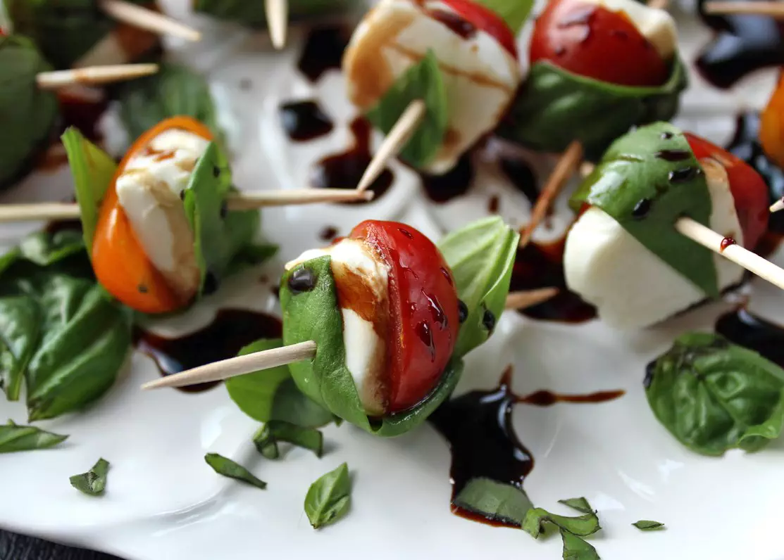 Cherry tomatoes and fresh mozzarella wrapped with fresh basil leaves on white plate