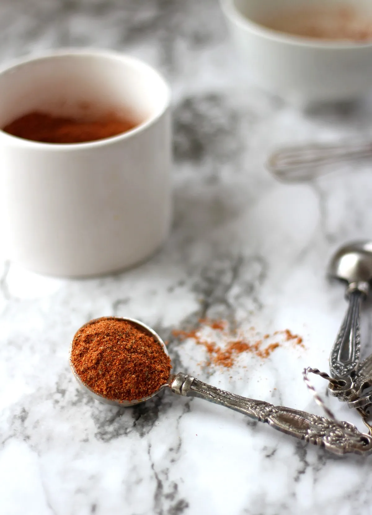 seasoning mix in a white container and some in a tablespoon on a marble background