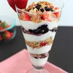 yogurt and berries layered with granola in clear fluted glass