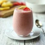 pink smoothie in clear glass with lemons and strawberries on cutting board in background