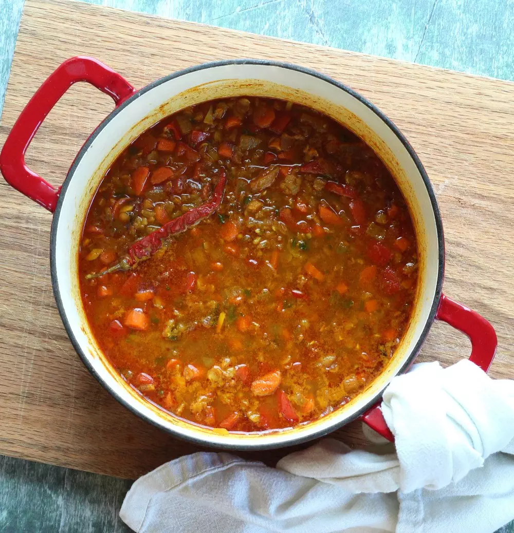 Unblended red lentil soup in pot on wood cutting board