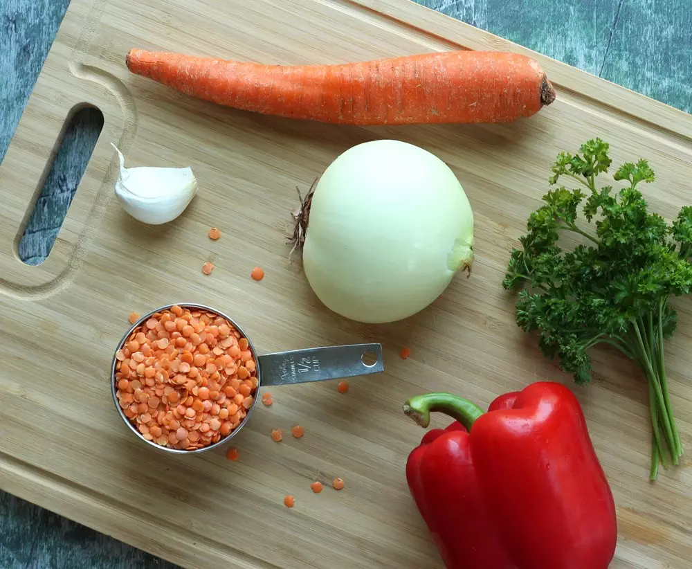 Carrot, onion, red pepper, red lentils, garlic, and parsley on wood cutting board